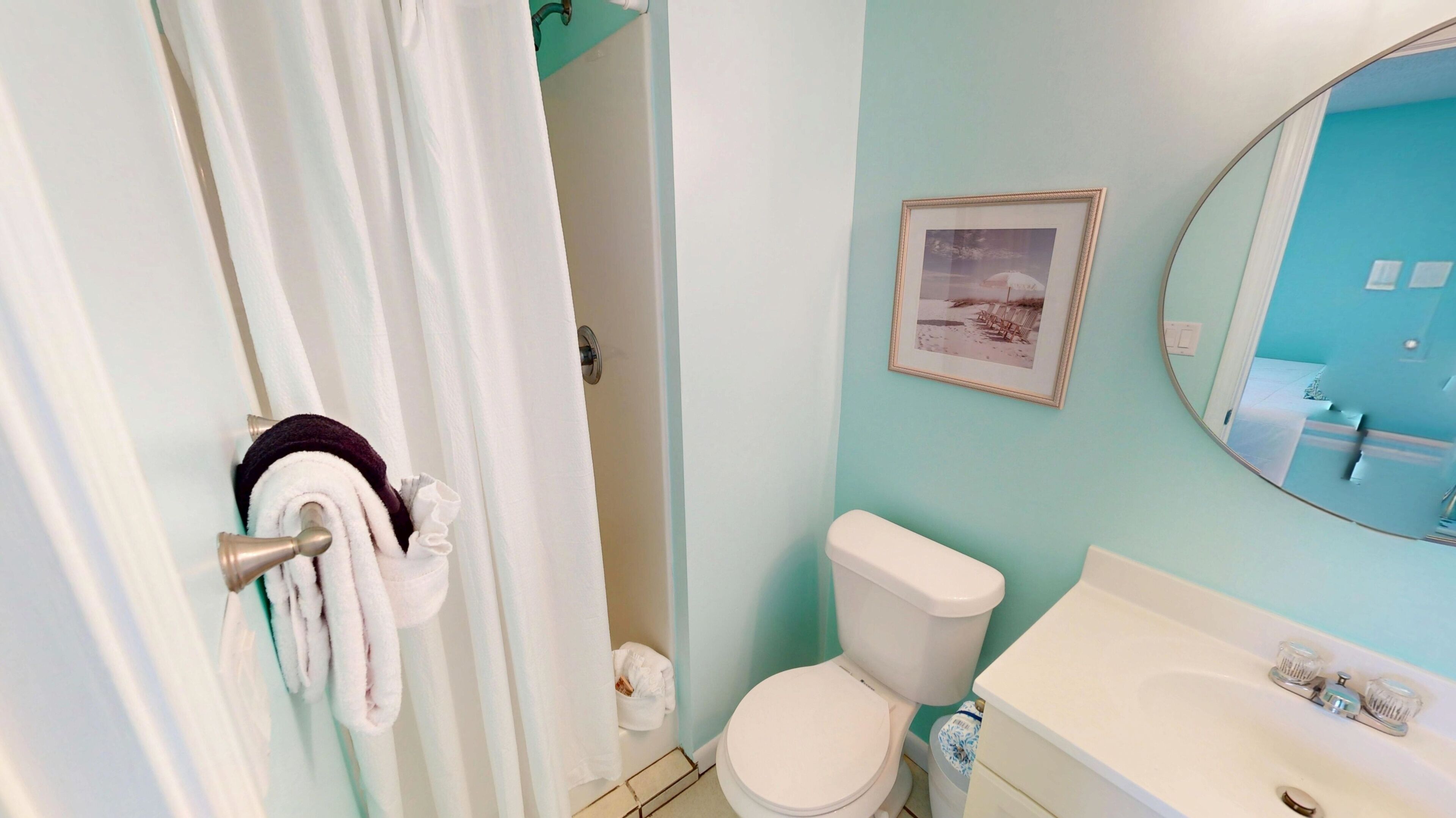 A bathroom with a toilet, sink, and a framed picture on the wall.