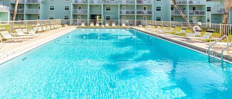 A swimming pool with lounge chairs and palm trees, surrounded by a multi-story building with balconies.