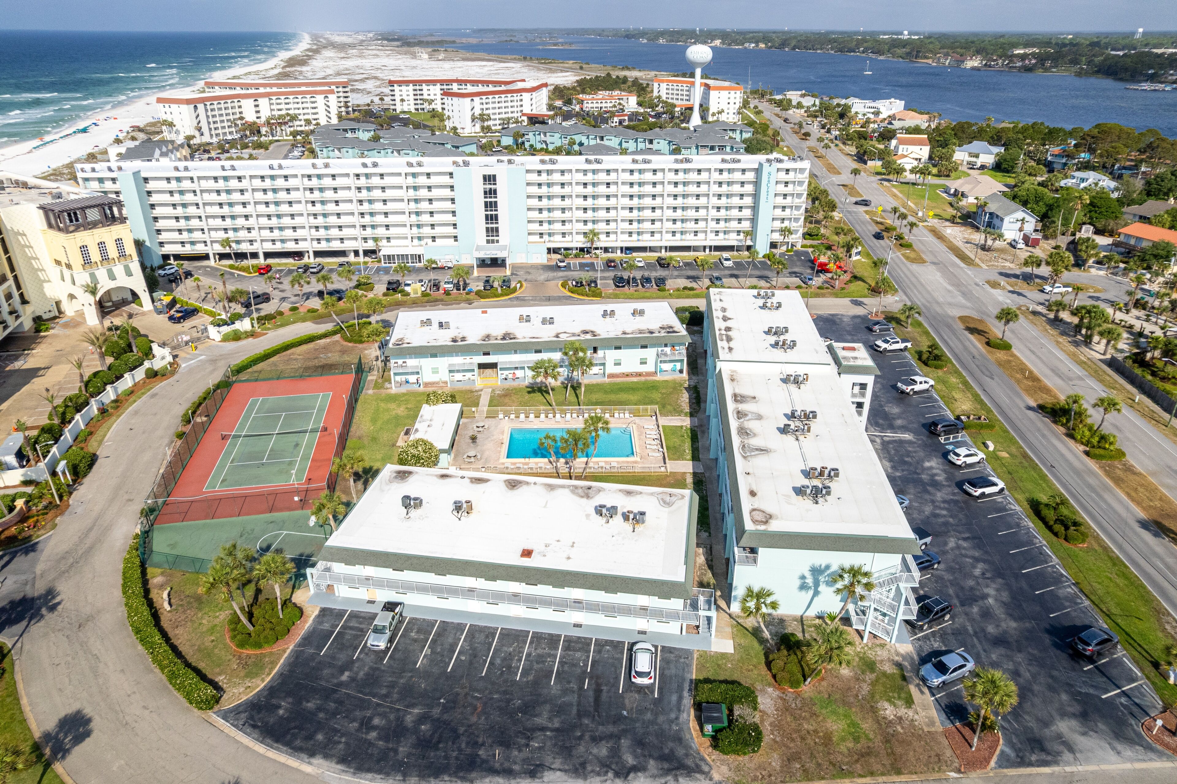 An aerial view of a hotel with multiple buildings, a tennis court, a swimming pool, and a parking lot.