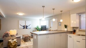 A modern kitchen with a central island, pendant lighting, and a dining area with a sofa and table. - Hip & Urban Condo near the heart of Old Town (Fort Collins)