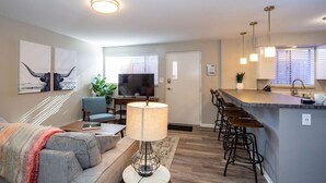 A modern living room with a sofa, a coffee table, a TV, and a bar area with stools. - Hip & Urban Condo near the heart of Old Town (Fort Collins)