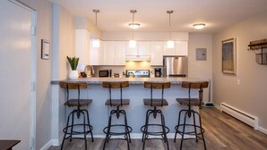 A modern kitchen with four bar stools, stainless steel appliances, and pendant lighting. - Hip & Urban Condo near the heart of Old Town (Fort Collins)