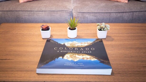 A book titled 'Colorado A Historical Atlas' on a wooden table with three small potted plants. - Hip & Urban Condo near the heart of Old Town (Fort Collins)