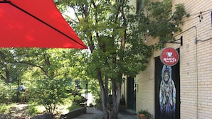An outdoor patio area with stone flooring, metal chairs, a red umbrella, and a mural on the building. - Cozy Carriage House | Walk to UNC | + Free Bikes (Greeley)
