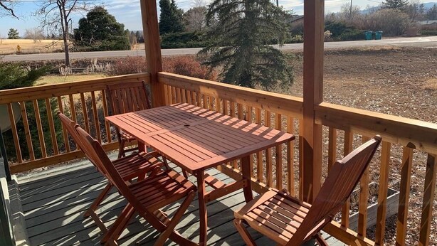 Una terraza de madera con una mesa y sillas, con vistas a un paisaje rural con árboles y una carretera.