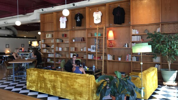 Una biblioteca amb prestatgeries, un sofà groc i un terra amb mosaic de quadradets.