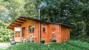 A wooden cabin with a chimney, a bench, and two potted plants.