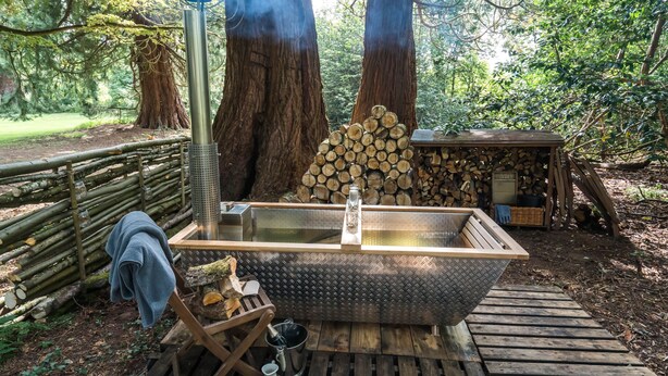 A hot tub in a forested area with a metal frame, surrounded by trees and a wooden deck.