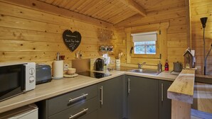 A wooden cabin-style kitchen with a microwave, toaster, kettle, and a heart-shaped welcome sign.
