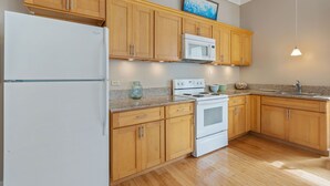 A kitchen with wooden cabinets, a white refrigerator, a microwave, a stove, and a granite countertop.