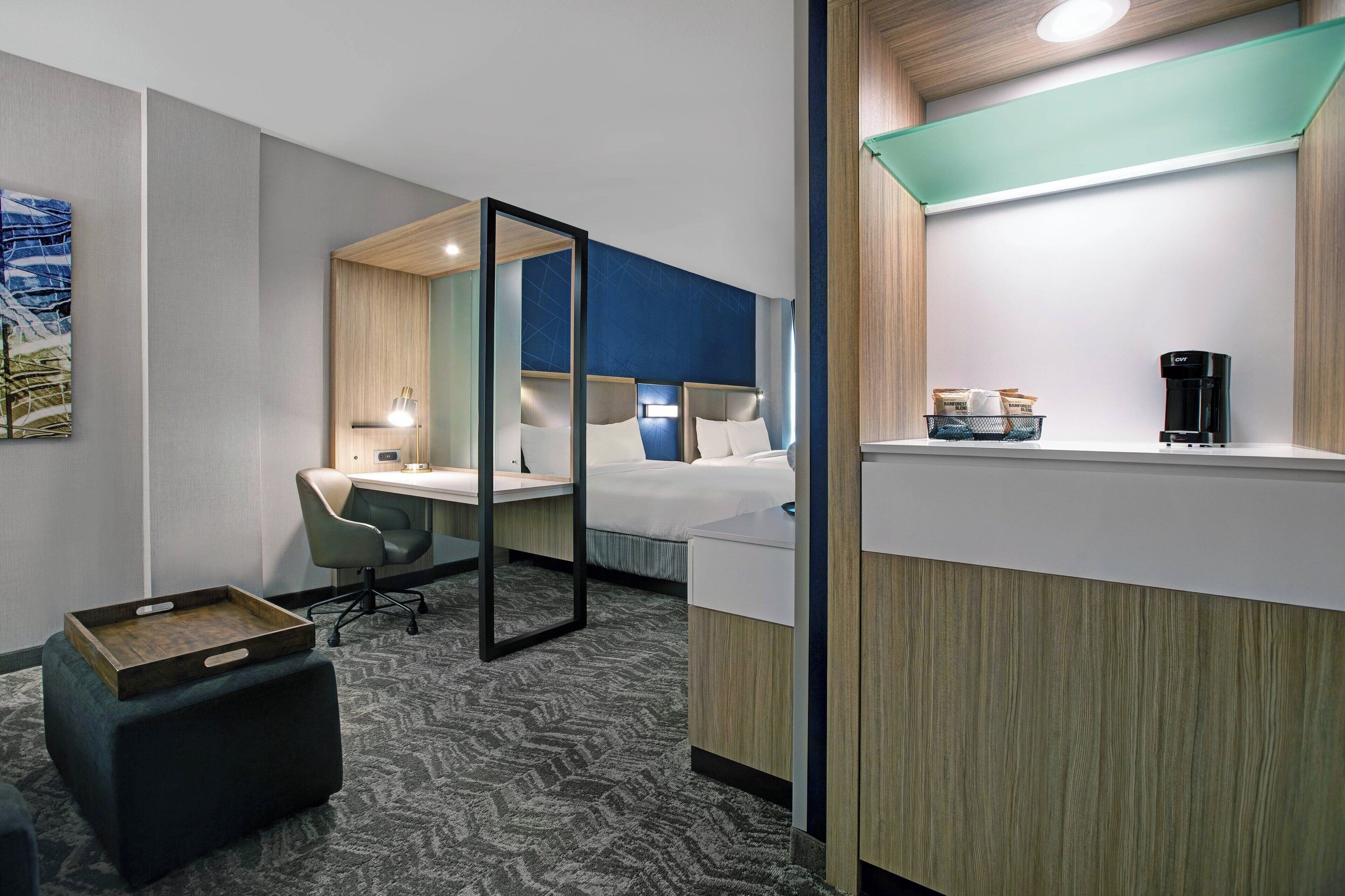 A hotel room with a bed, desk, chair, and a coffee machine.