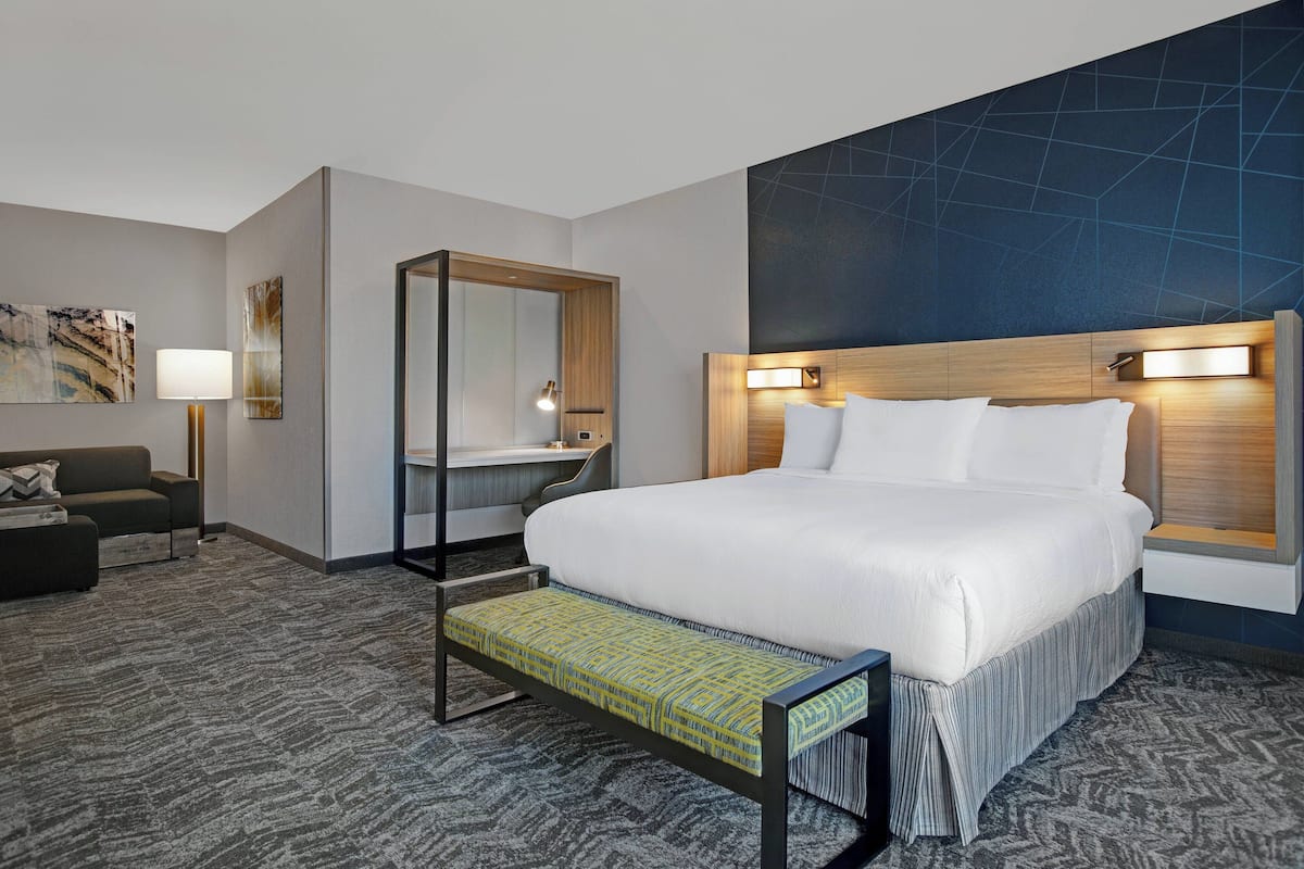 A hotel room with a large bed, a desk, a mirror, and a sofa.