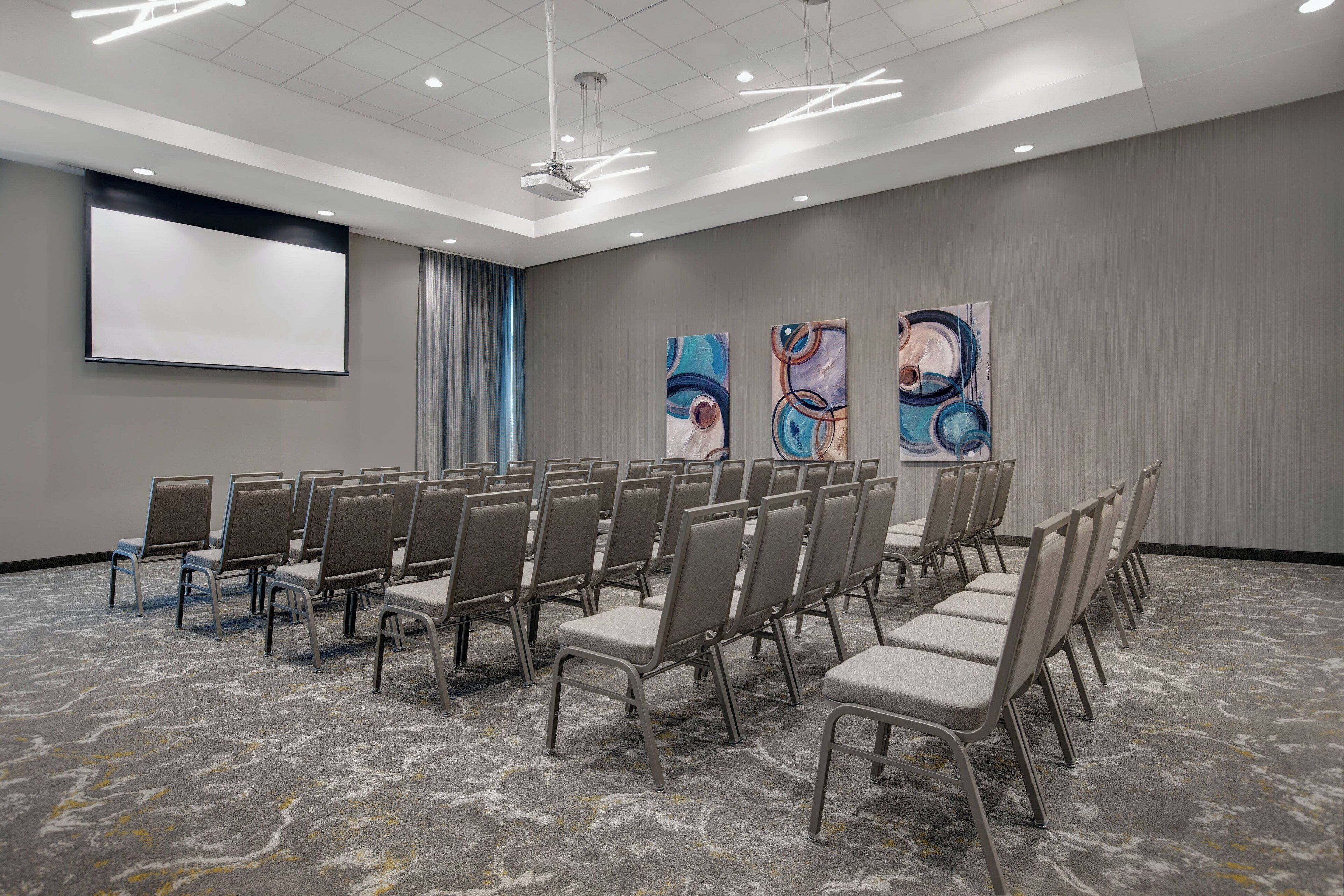 A conference room with rows of chairs, a projector screen, and abstract art on the walls.