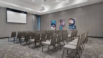 A conference room with rows of chairs, a projector screen, and abstract art on the walls.