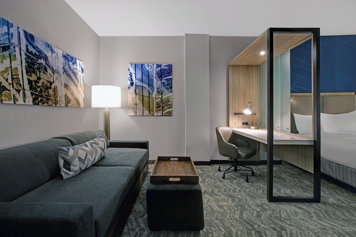 A hotel room with a sofa, a desk, a chair, a bedside table, and a bed.