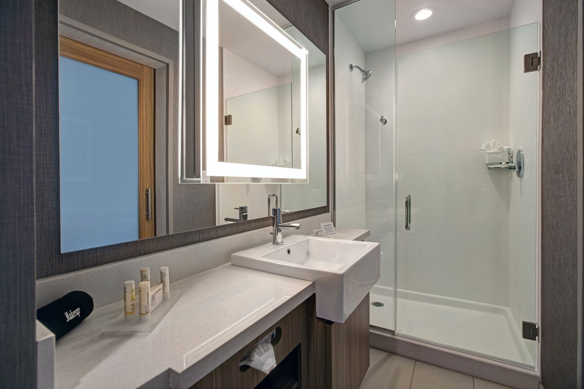 Une salle de bain moderne avec un grand miroir, deux lavabos, une douche et un porte-serviettes.