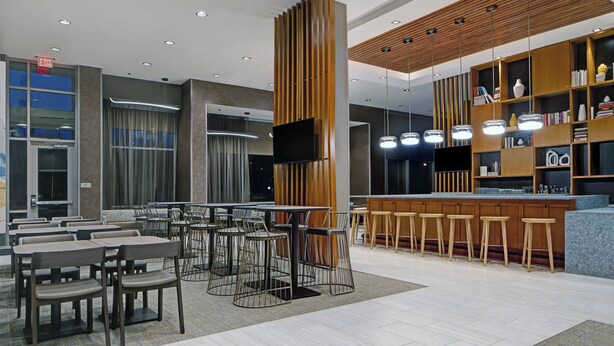 Un restaurant moderne doté d’un bar, de différents types de sièges, notamment des tables et des tabourets, ainsi que d’un écran de télévision.