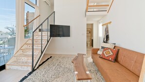 Un salon moderne avec un escalier, un téléviseur à écran plat, un banc en bois et un canapé marron agrémenté de coussins à motifs.