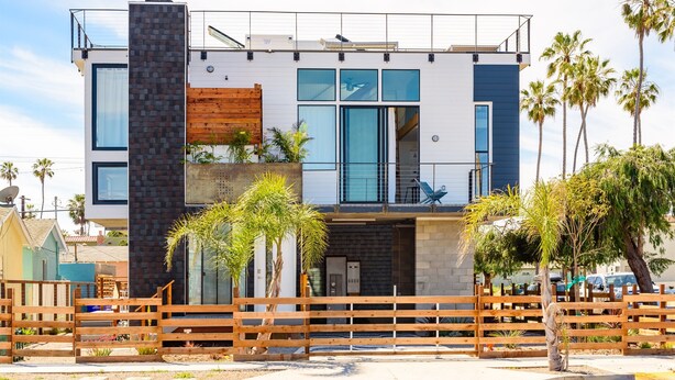 Une maison moderne à deux étages, dotée d’un balcon, de grandes fenêtres et d’une clôture en bois dans le jardin avant.