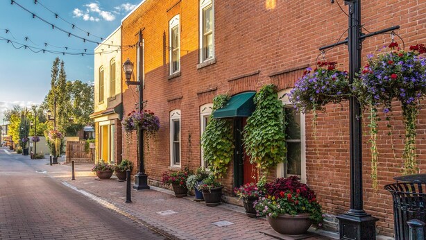 A brick building with large flower pots on the sidewalk, a street lamp, and a hanging flower basket. - FireHouse Alley Elegant Loft-Style Retreat (Fort Collins)