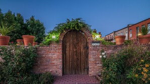 A brick wall with a wooden door, potted plants, and a brick pathway leading to a building. - FireHouse Alley Elegant Loft-Style Retreat (Fort Collins)