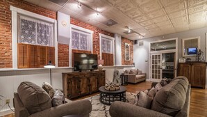 A cozy living room with a brick wall, wooden shutters, a television, and a sofa. - FireHouse Alley Elegant Loft-Style Retreat (Fort Collins)