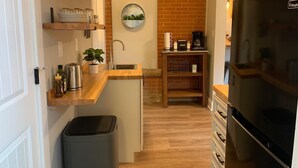 A compact kitchen with wooden shelves, a sink, a refrigerator, and a coffee maker. - Gorgeous Guest Suite. Walk to Old Town & CSU! (Fort Collins)