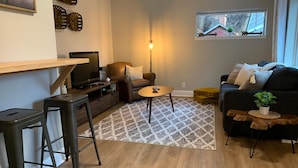 A living room with a TV, sofa, coffee table, and a window with a view of a house. - Gorgeous Guest Suite. Walk to Old Town & CSU! (Fort Collins)