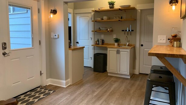 A compact kitchen with white cabinetry, wooden countertops, and built-in shelves. There is a black trash bin and a wooden stool near the sink. - Gorgeous Guest Suite. Walk to Old Town & CSU! (Fort Collins)