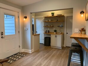 Compact kitchen with central island and upper cabinets, featuring a light-colored countertop and wooden shelving above the sink.