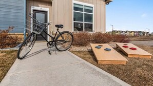 Un bâtiment devant lequel est garé un vélo, une porte portant l’inscription « D », et deux tables en bois avec des coussins.