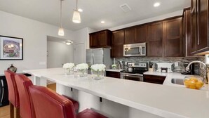 Une cuisine moderne avec des meubles en bois foncé, des appareils en acier inoxydable et un îlot central blanc agrémenté de tabourets de bar rouges.