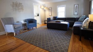 Ein Wohnzimmer mit grauem Sessel, blauem Sessel, dunklem Sofa und einem gemusterten Teppich.