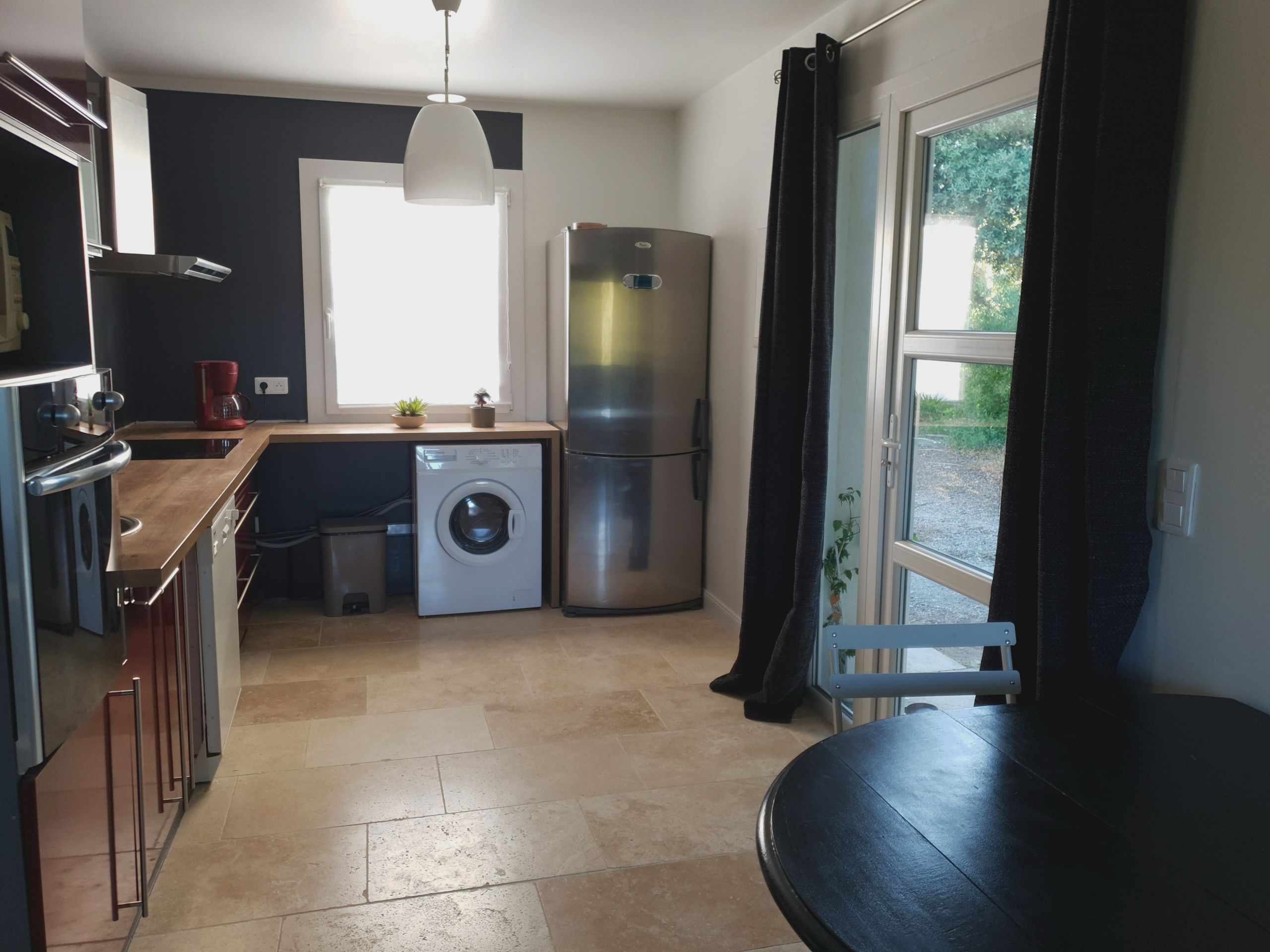 Een kleine keuken met een wasmachine, een koelkast en een raam met gordijnen.