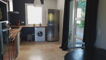 Een kleine keuken met een wasmachine, een koelkast en een raam met gordijnen.