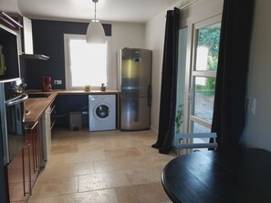 Una cocina pequeña con lavadora, refrigerador y una ventana con cortinas.