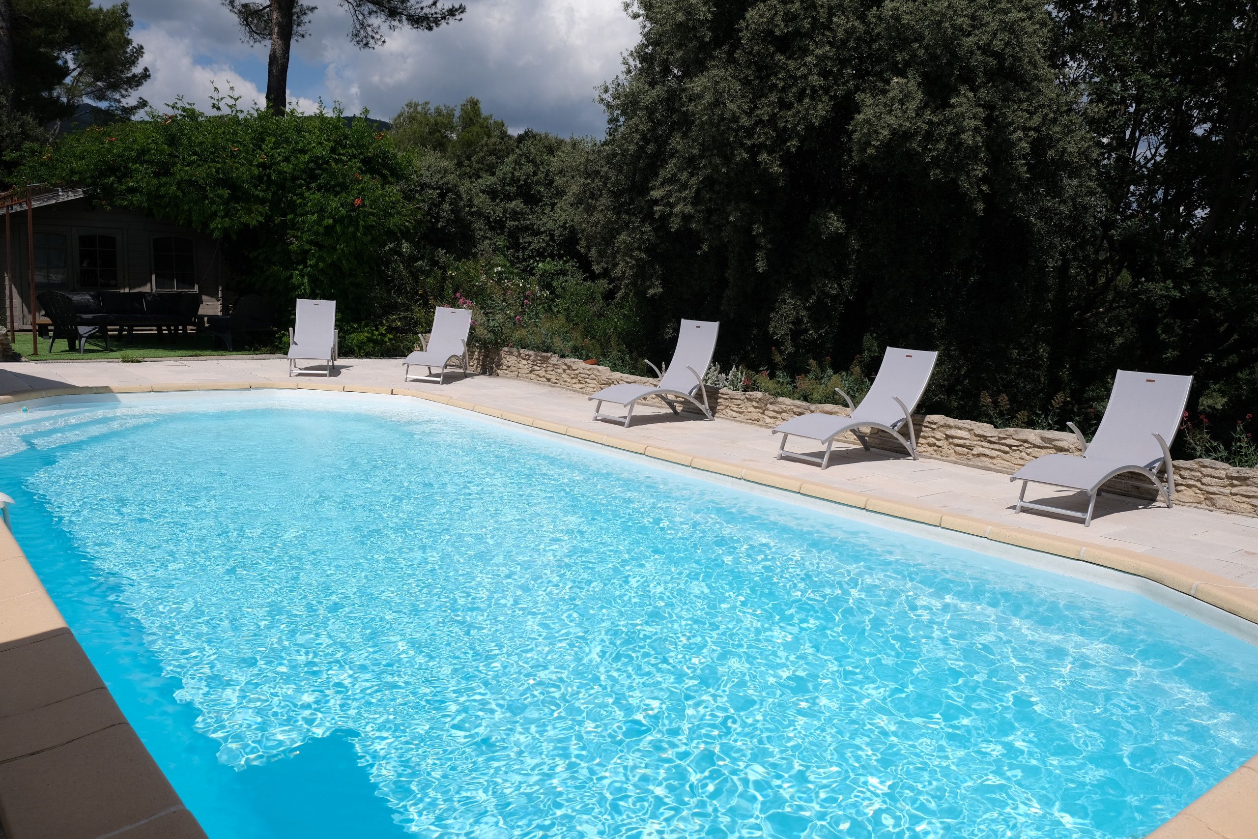 A swimming pool with clear blue water, surrounded by lounge chairs and a stone wall.