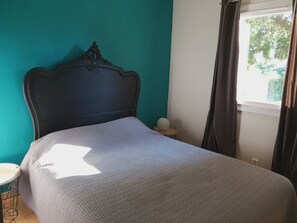 A bed with a dark headboard, a grey blanket, and a small round object on a wooden stool beside it.