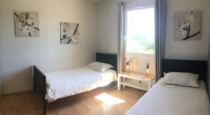 A bedroom with two single beds, a window with curtains, and two wall-mounted artworks.