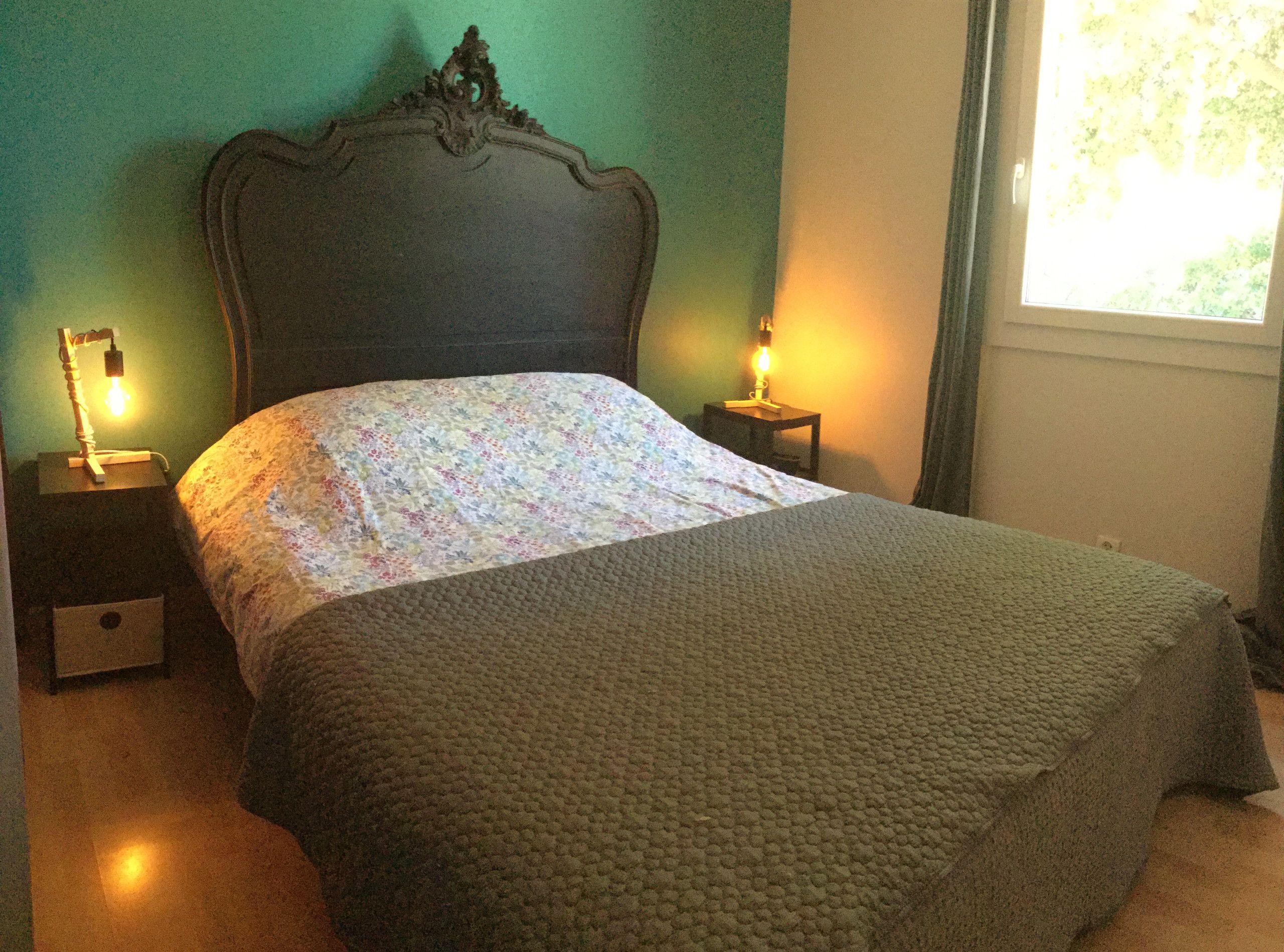 Een bed met een bloemenprint, twee nachtkastjes met lampen, een nachtkastje met lade en een raam met gordijnen.