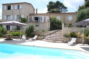 A pool area with lounge chairs and umbrellas, a stone staircase, and a building with multiple windows and balconies.