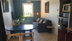 A compact living space with a dining table, chairs, a sofa, a small side table, a potted plant, a hanging light fixture, a clock, and a microwave. - Vacation rental house with pool PUGET LS2-356 (Puget)