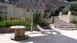 A patio area with a round wooden table, two white lounge chairs, and a large umbrella. - Vacation rental house with pool PUGET LS2-356 (Puget)