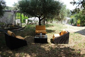 An outdoor seating area with wicker furniture and a small table, surrounded by greenery and a tree. - Vacation rental house with pool PUGET LS2-356 (Puget)