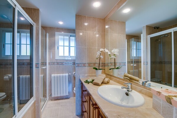 Une salle de bain moderne avec une douche à l’italienne en verre, un grand lavabo avec un miroir et deux orchidées en pot.