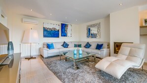 A modern living room with a glass coffee table, white sofas, and blue cushions. - Luxurious house near sea Barcares Nou Alcudia (Alcúdia)
