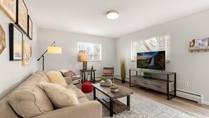 Una sala de estar con sofá, mesa de centro, televisor y cuadros en la pared.