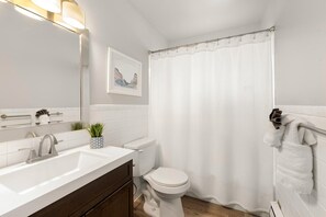 A bathroom with a white sink, a toilet, a shower curtain, a towel rack, and a framed picture on the wall.