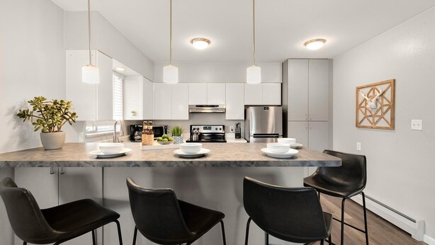 Una cocina moderna con armarios blancos, una isla central con taburetes de bar, electrodomésticos de acero inoxidable e iluminación colgante.