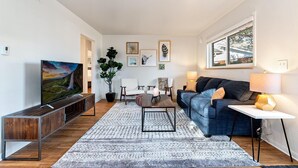 A modern living room with a TV, sofa, coffee table, and artwork on the walls. - Hidden Gem Near Old Town, BBQ & Bikes!! (Fort Collins)
